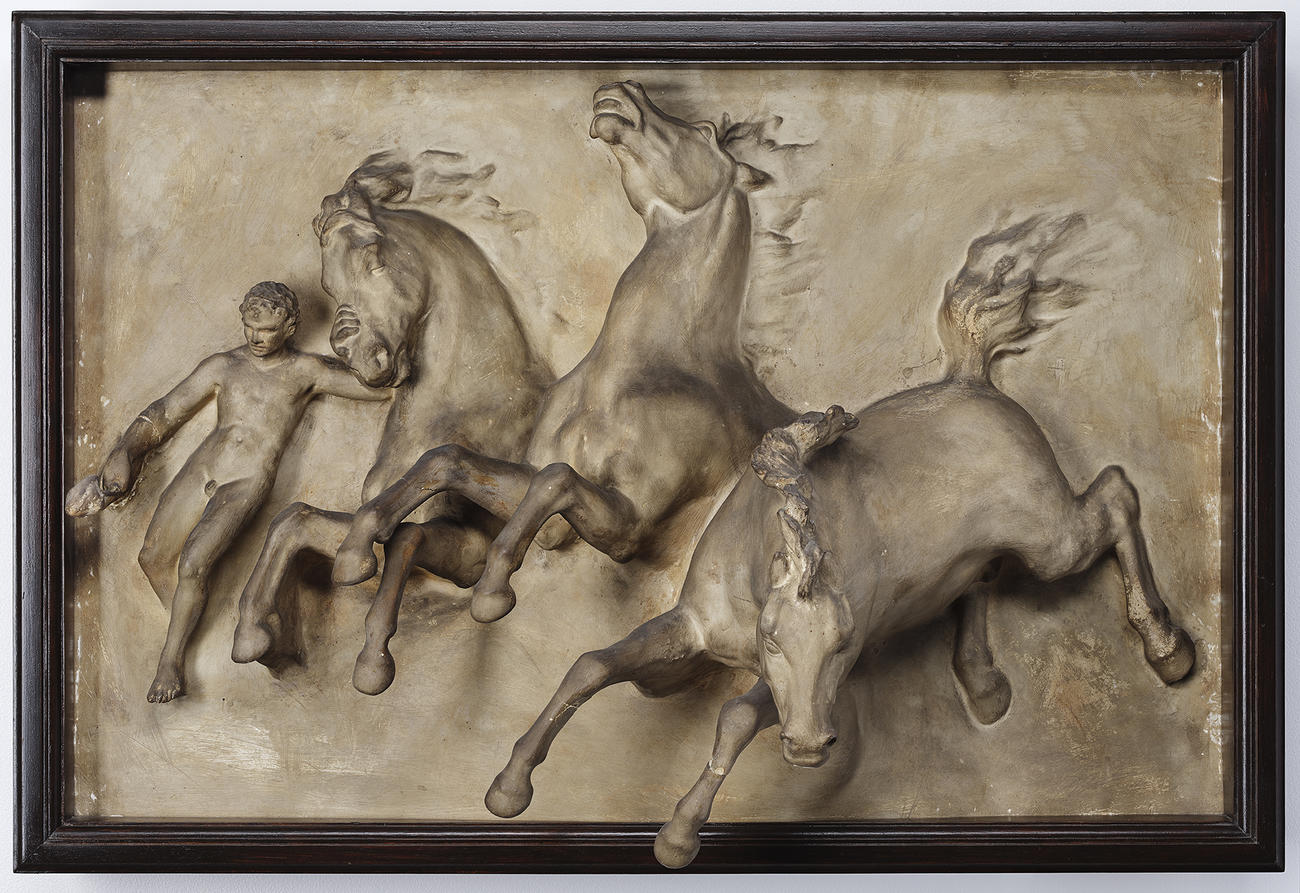  A plaster cast of three charging horses alongside a human figure. The surface is covered in dark grime. 
