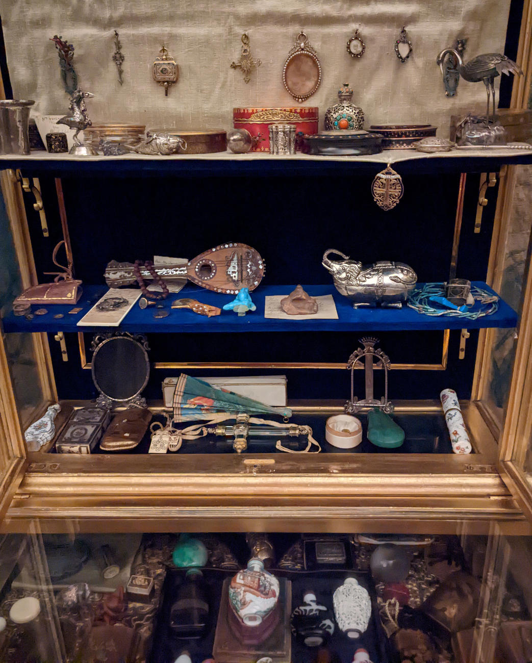 An image of a gilt vitrine from the Gardner Museum showing four levels of small objects displayed in its interior.