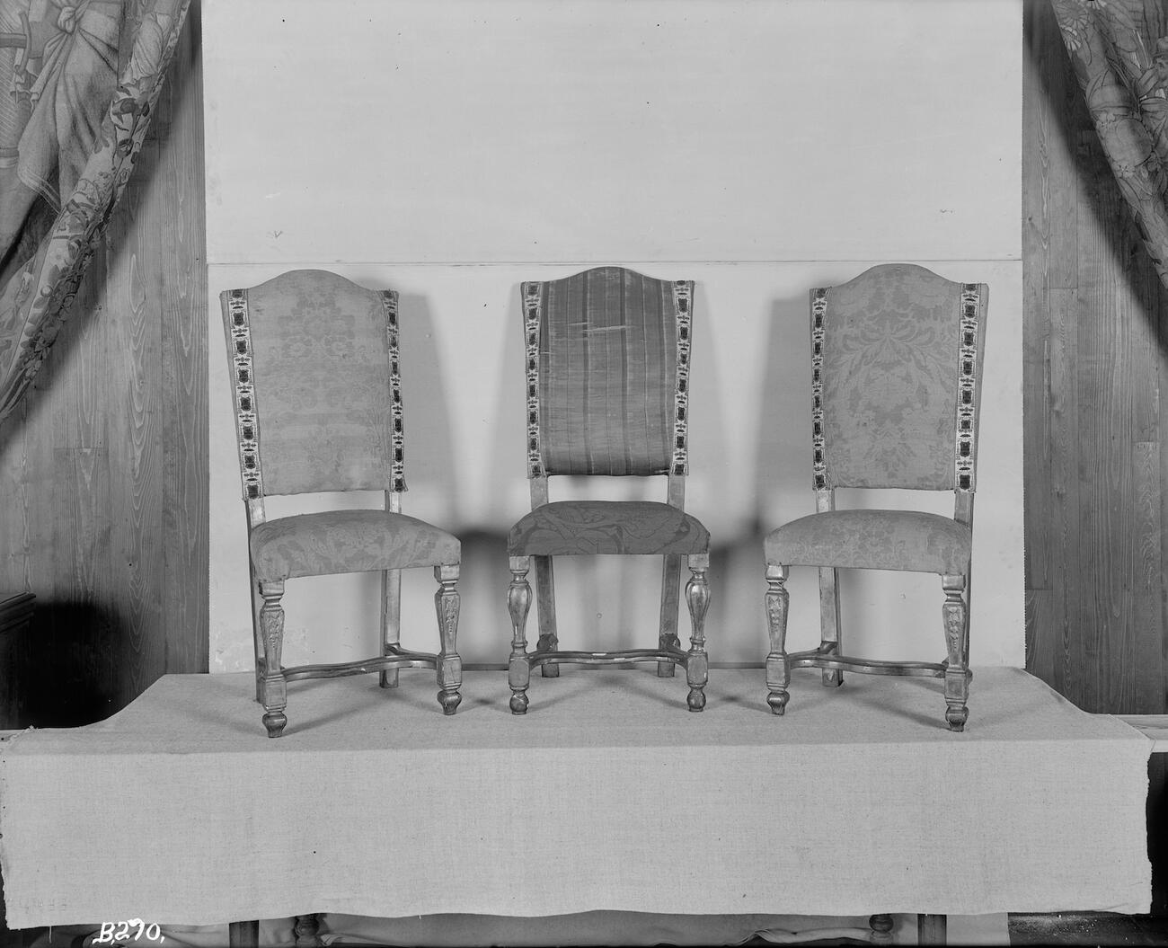 Black and white photograph of three chairs laid over a colorized photograph. The fabric on the middle chair is pink striped.