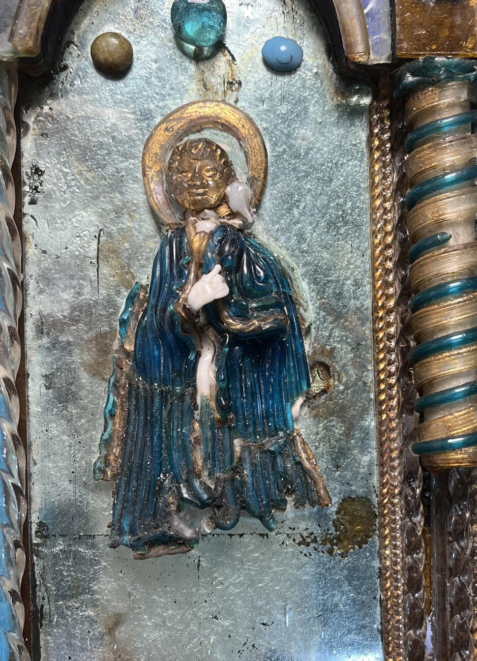 Detail of a saint on the Black Glass Madonna with gold face and halo and turquoise blue robe, showing the contrast between the before treatment with dirty and missing pieces and after with glass fragments have been reattached and missing pieces have been filled with the paper tubes.