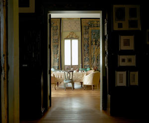 A doorway entering into a sitting room with white chairs and ornate tapestries on the walls. 