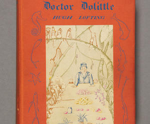 A photograph of a hardcover version of The Story of Dr. Dolittle by Hugh Lofting, showing a human figure sitting at table surrounded by a variety of animals.