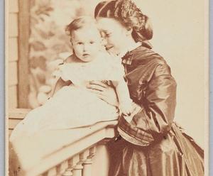 A sepia toned photograph of a white woman with dark hair and 19th century dress smiling and holding a baby. The woman, Isabella Stewart Gardner, is nuzzling the head of her son, Jackie.