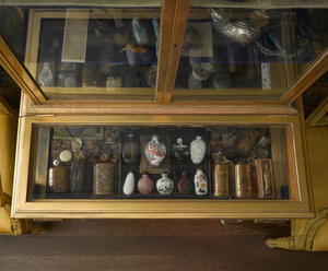 A shelf in a historic gilded, glass-door, cabinet with snuff bottles in the Little Salon of the Gardner Museum.