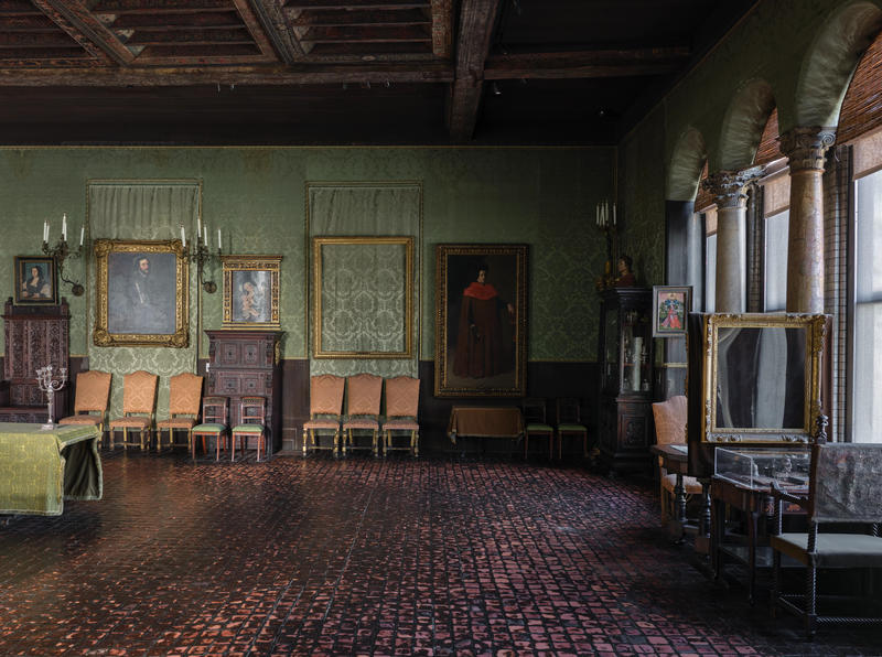 The wall of a room with green fabric and paintings and sculptures, and three empty frames.