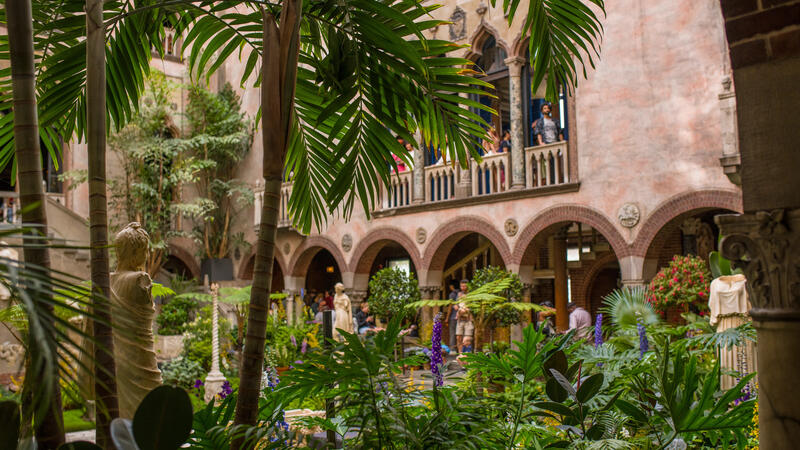 A view of the courtyard with palm trees on the left looking up towards a balcony. 