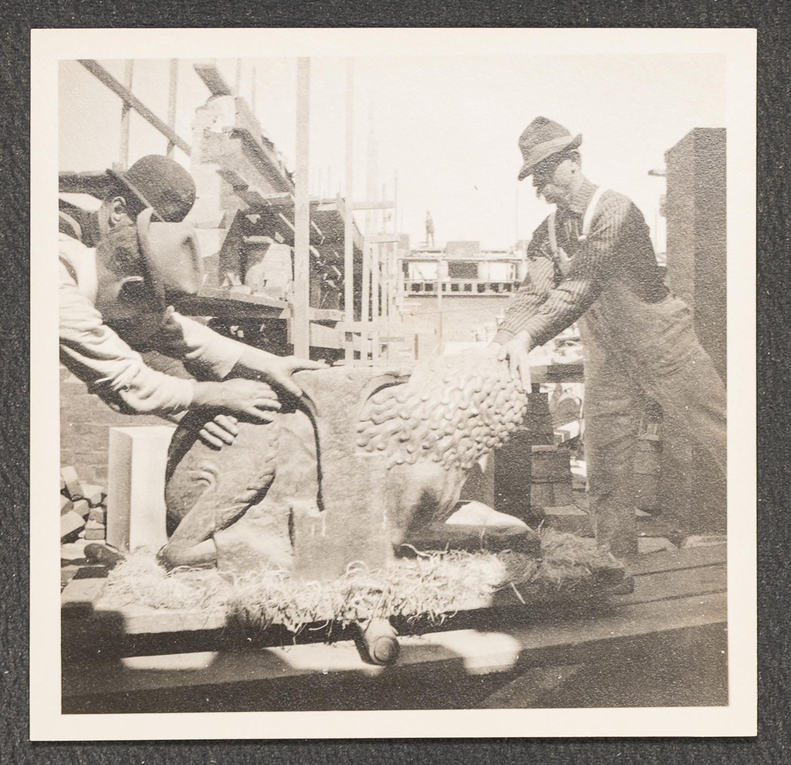 A black and white photograph of the Gardner Museum construction site with three men handling a stone sculpture.