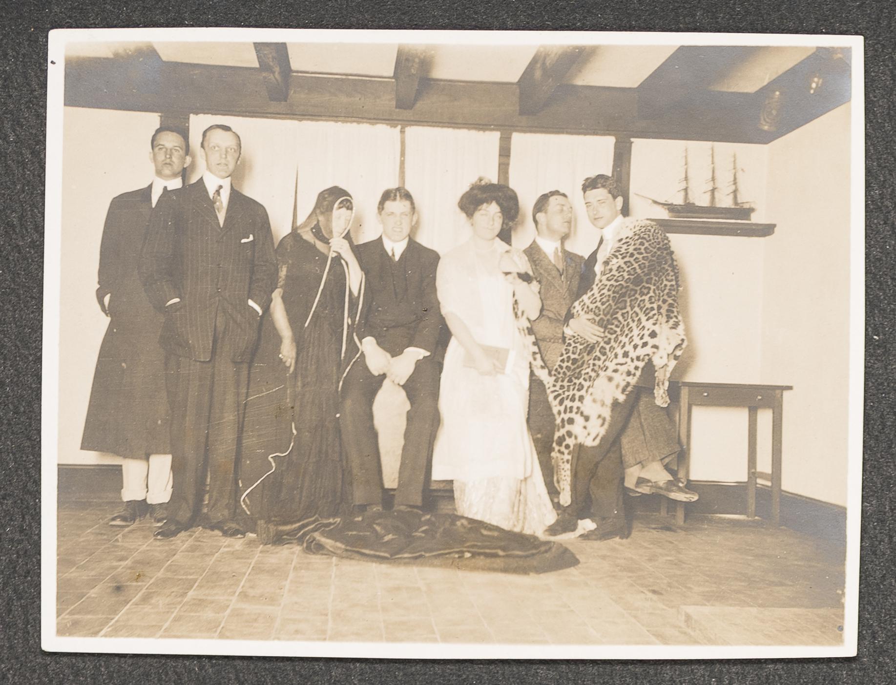 Black and white photo of 7 people, one wearing a tiger pelt