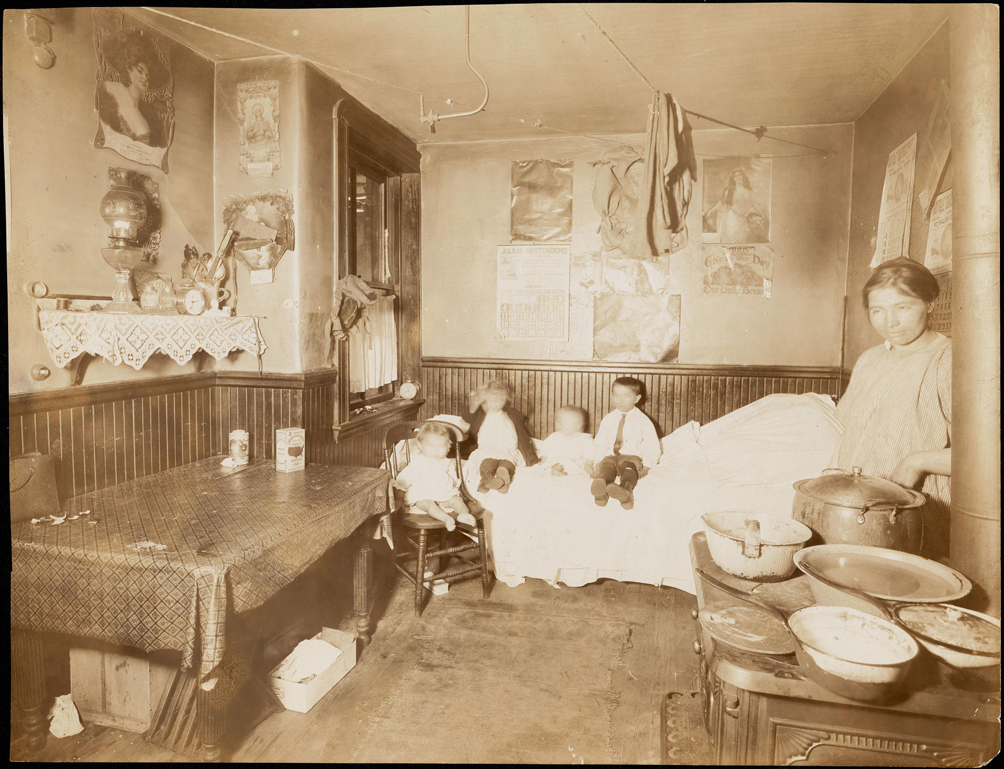 A sepia photo of a woman in an apartment with several children sitting on a bed.