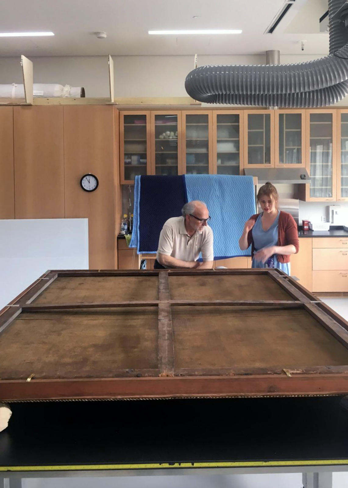 Two conservators standing over the back of a painting. 