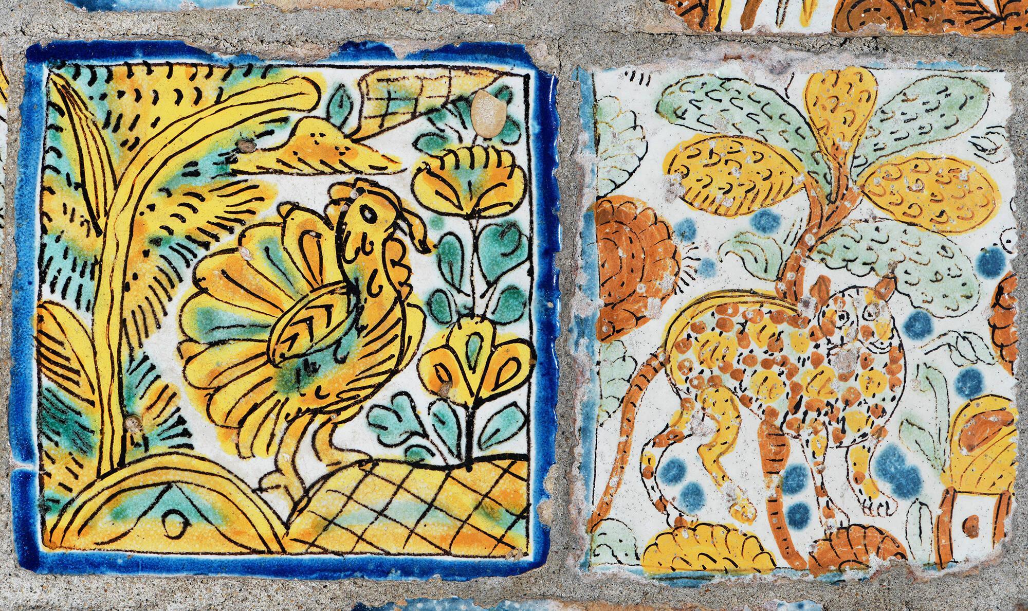 A tile with a bird painted on it on the left and a tile with a big cat painted on it on the right.