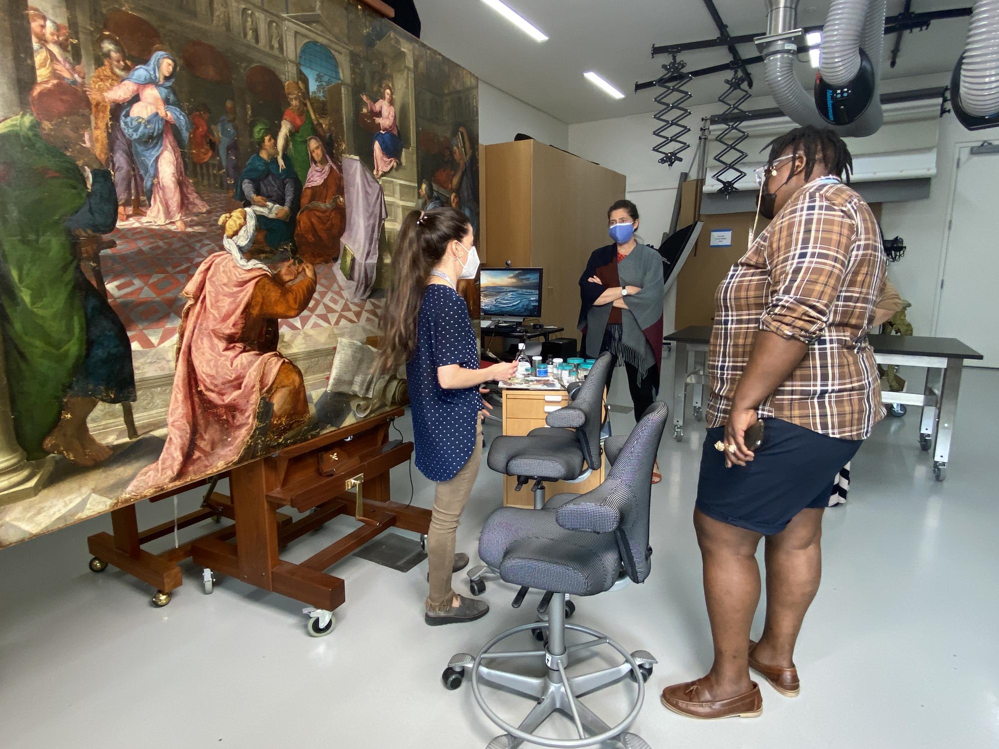 Porsha Olayiwola talks to conservators with a colorful painting behind them.