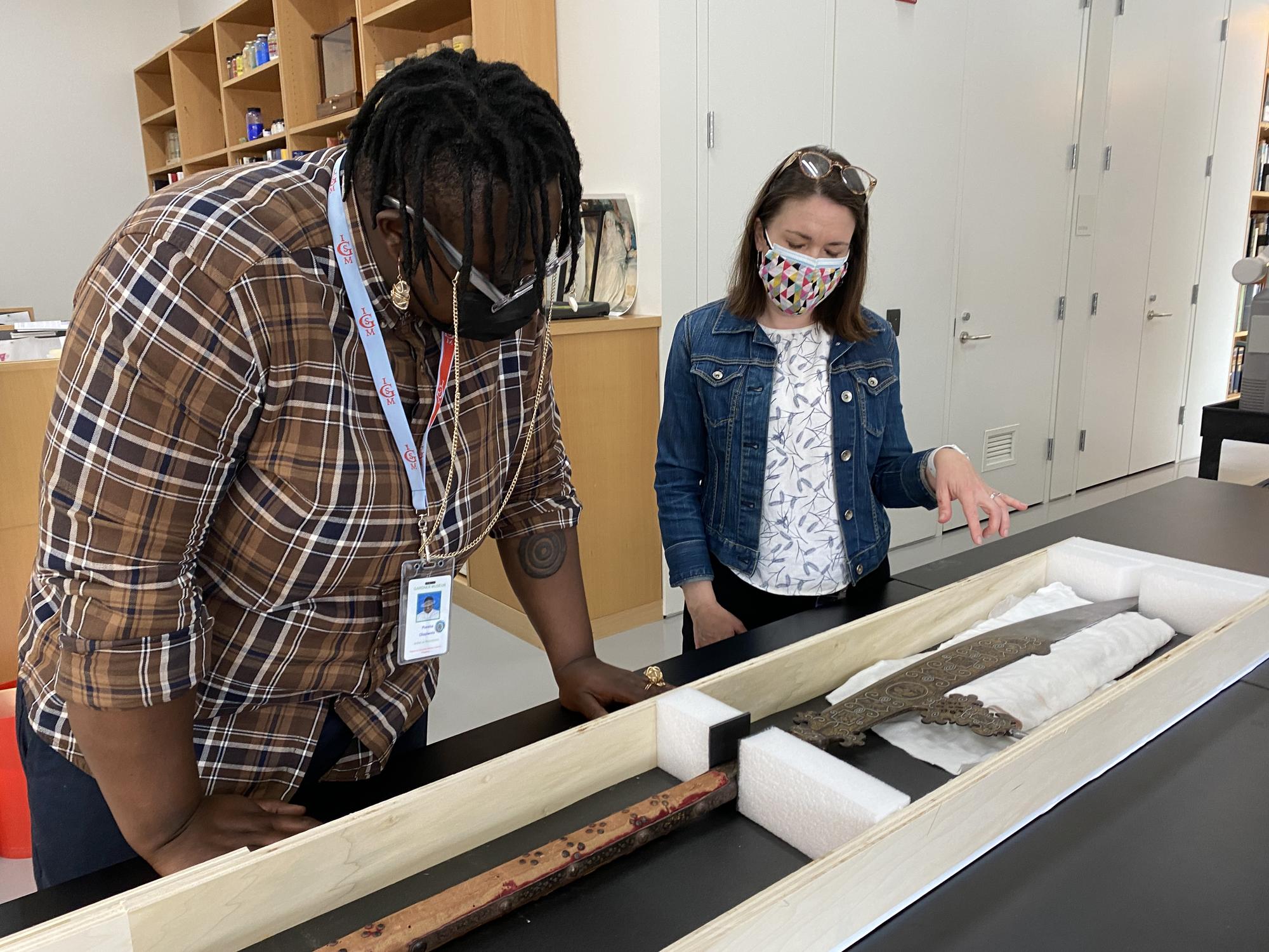 Porsha Olayiwola takes a closer look at an old pole-arm with a knife at one end of it encased in wood. 