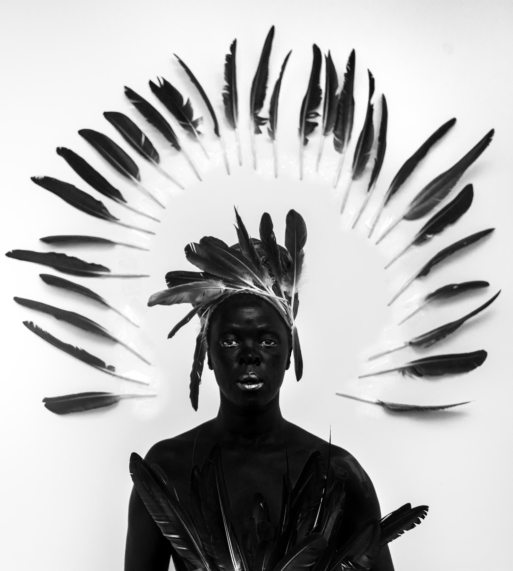 A person stands with black feathers on their body and white feathers shaped in a semi-circle around their head.