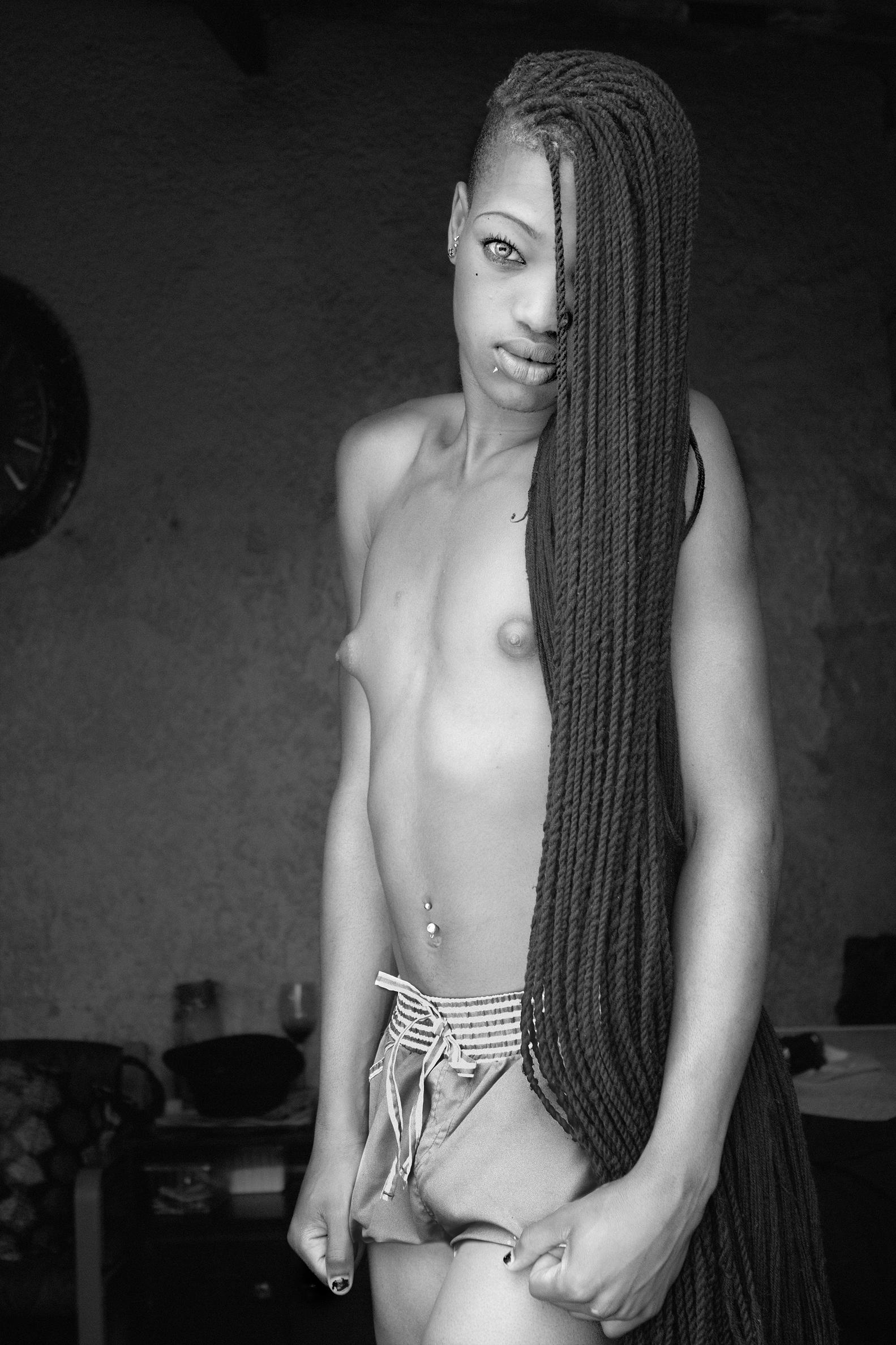 A photograph of a person with long braids, topless and in shorts. 