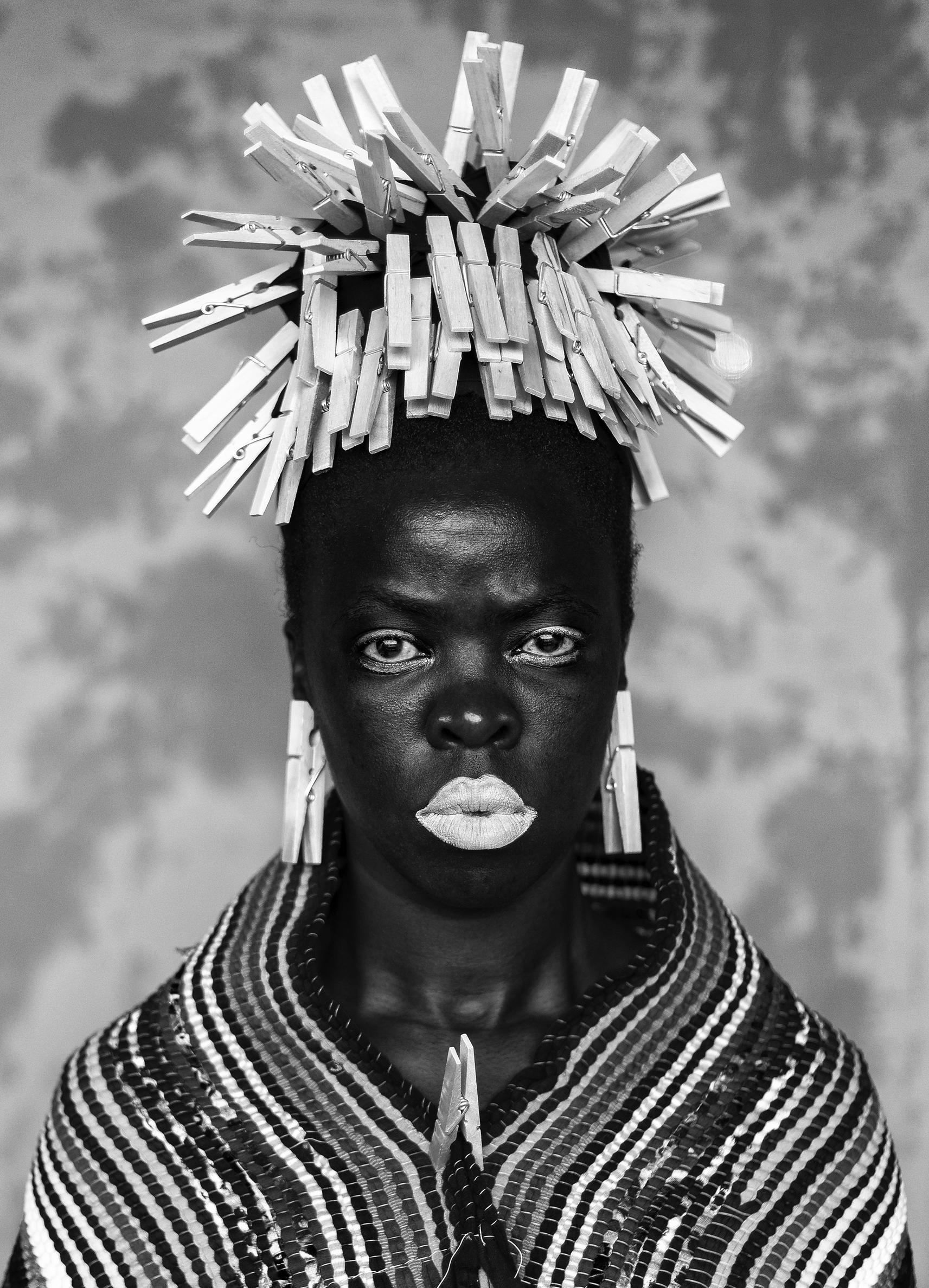 A black and white image of a person with white lipstick and clothes pins as earrings and hairpieces.