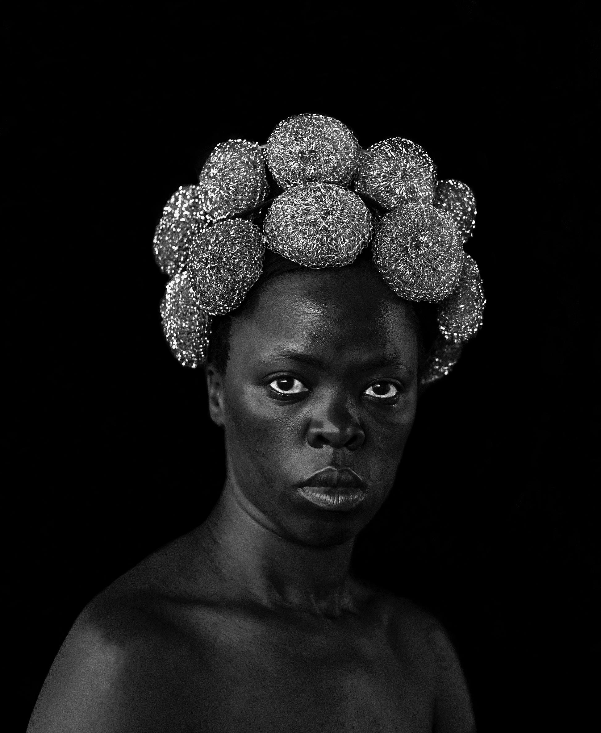 A black and white image of a person with a crown of circular flowers surrounding their hair.