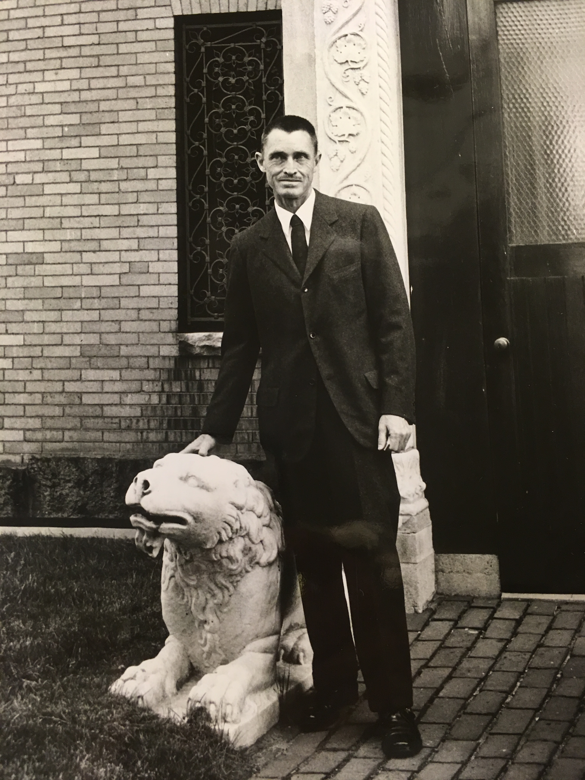 A black and white image of George Stout standing next to a stone lion.