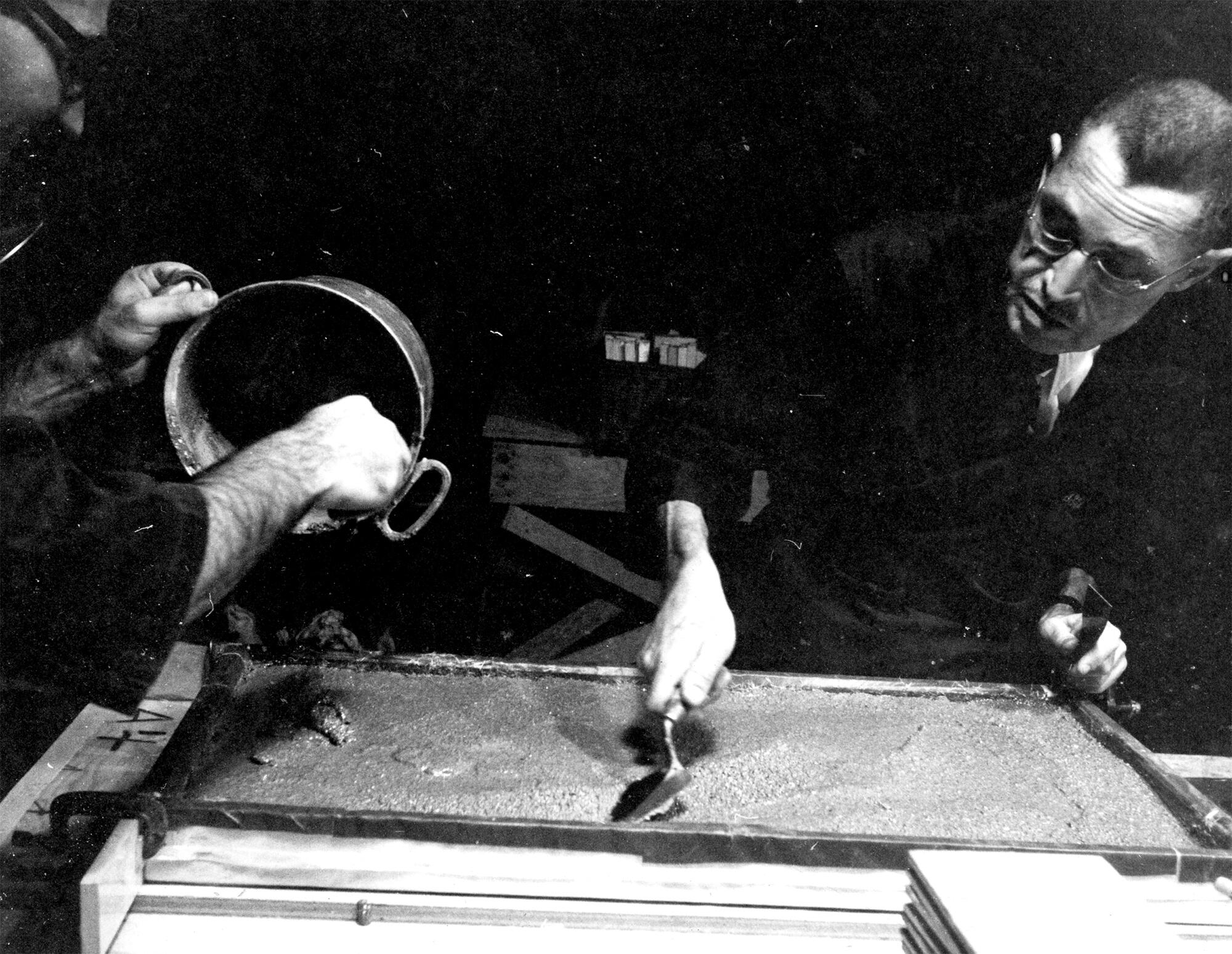 A black and white photo of George Stout working on a mosaic. 