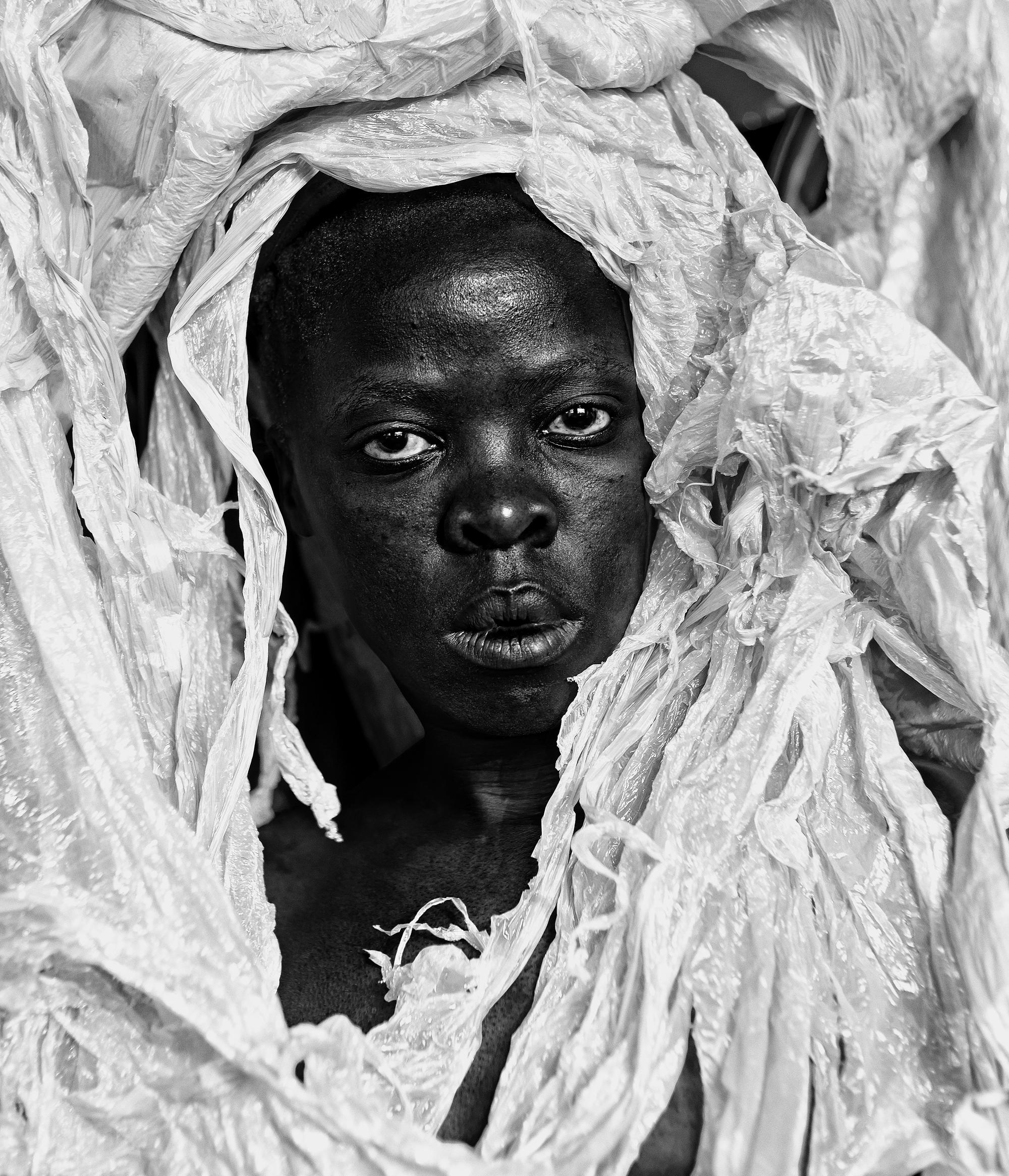 A black and white image of a person covered in tattered white cloth with only their face showing.