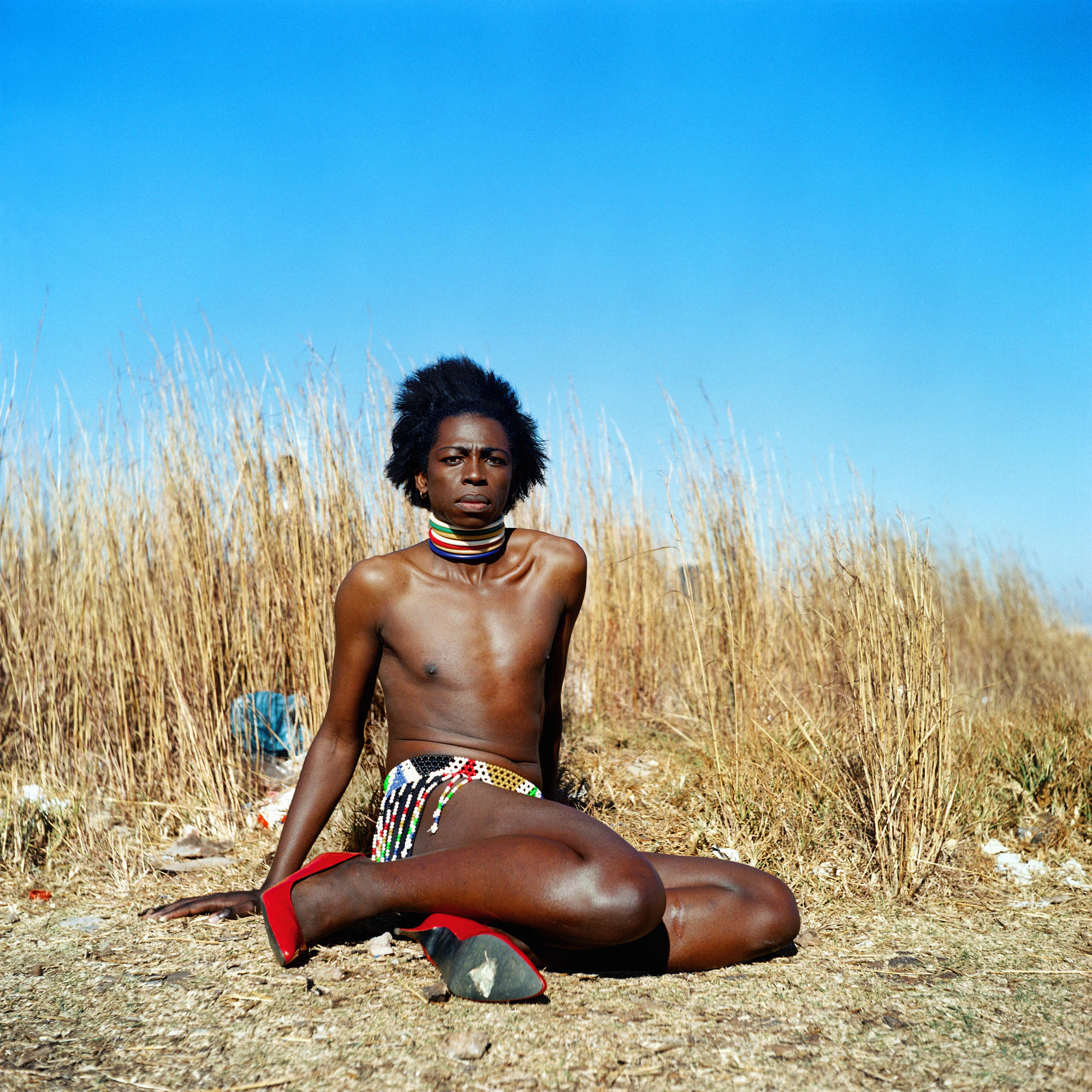 A person sits on the ground with a skirt and heels. 