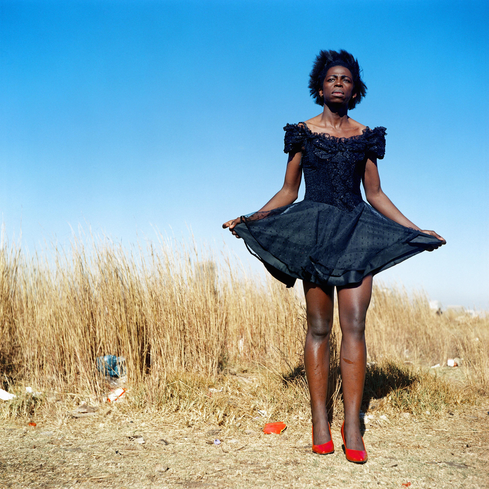 A person stands in a field in a blue dress.