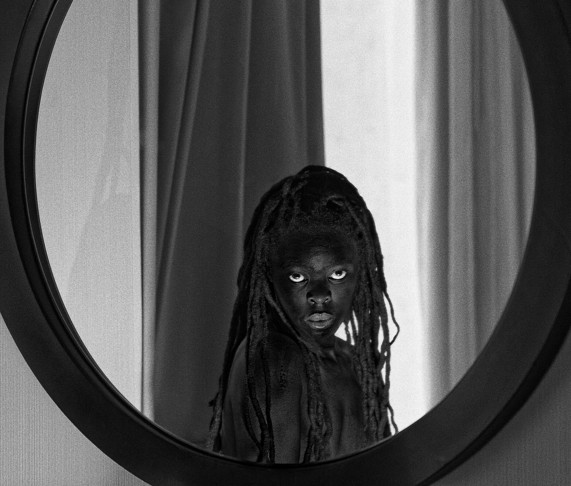 A black and white image of a person looking in a large mirror mounted on a wall.