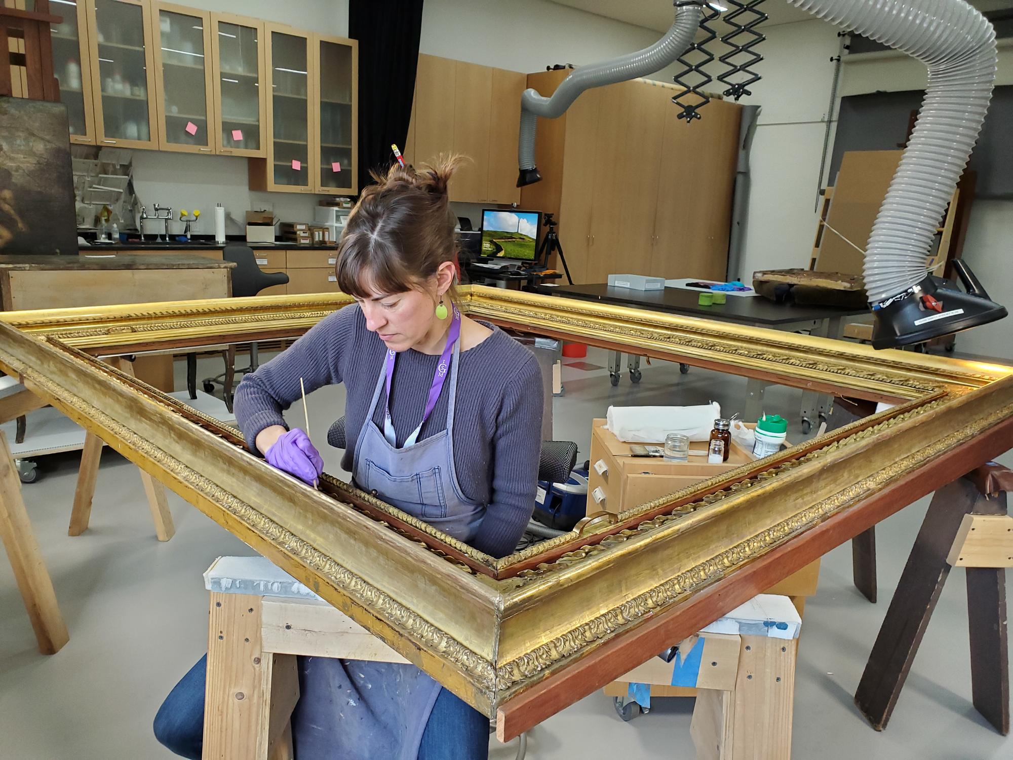 Allison Jackson cleaning a portion of a large golden frame. 
