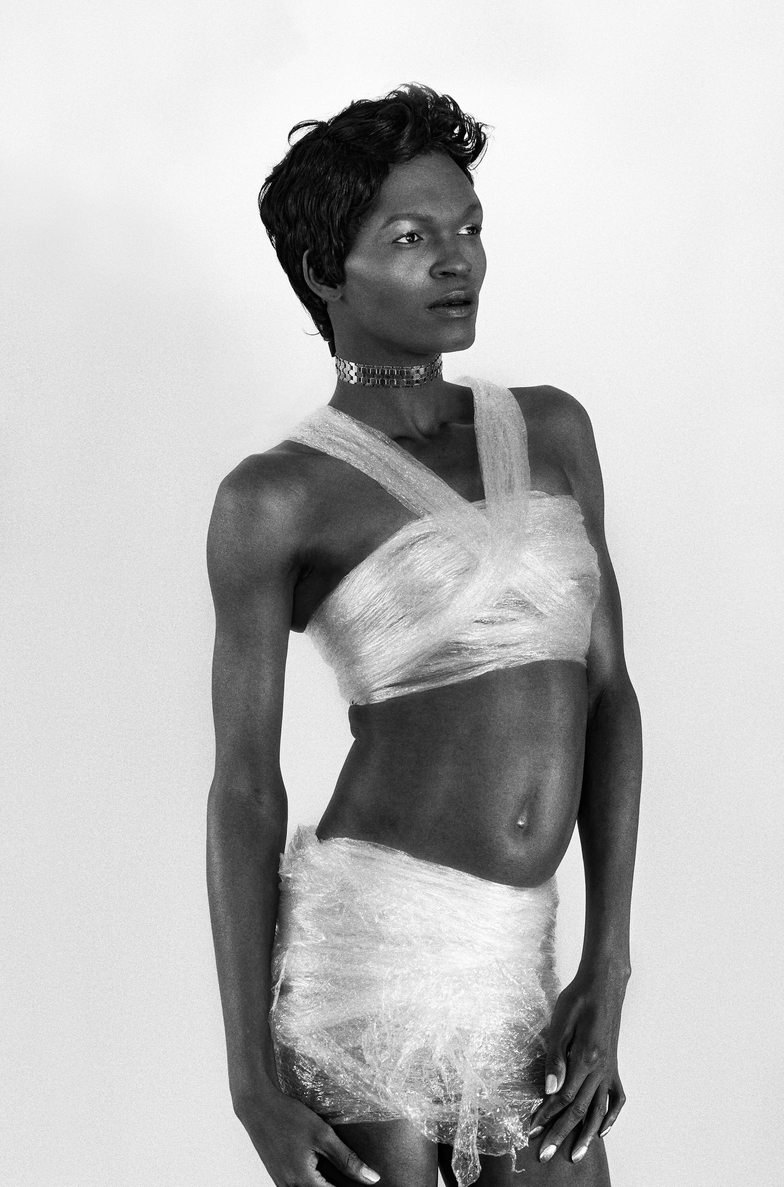 A black and white image of a person with saran wrap around them styled as a top and skirt.
