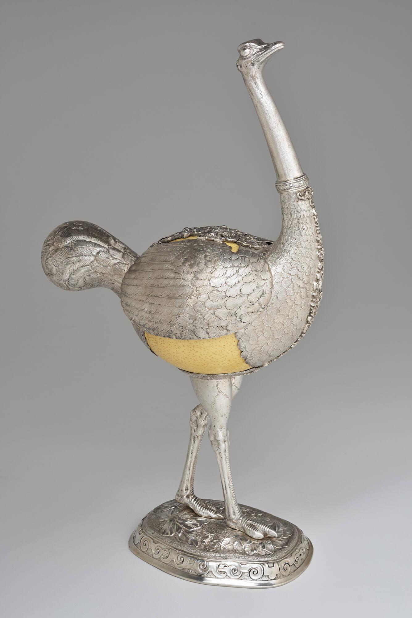  A silver sculpture of an ostrich with an creamy-white ostrich egg used as the body of the bird.