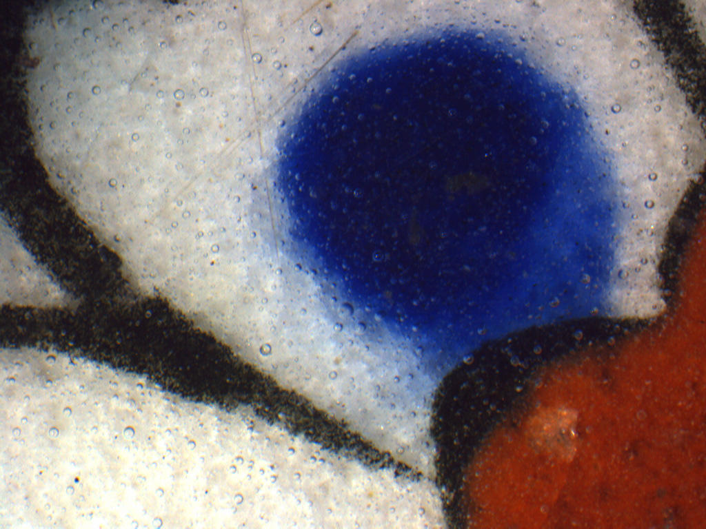 A magnified view of the Turkish tile showing the bubbles of the clear glaze top layer over areas of blue, red, white, and black
