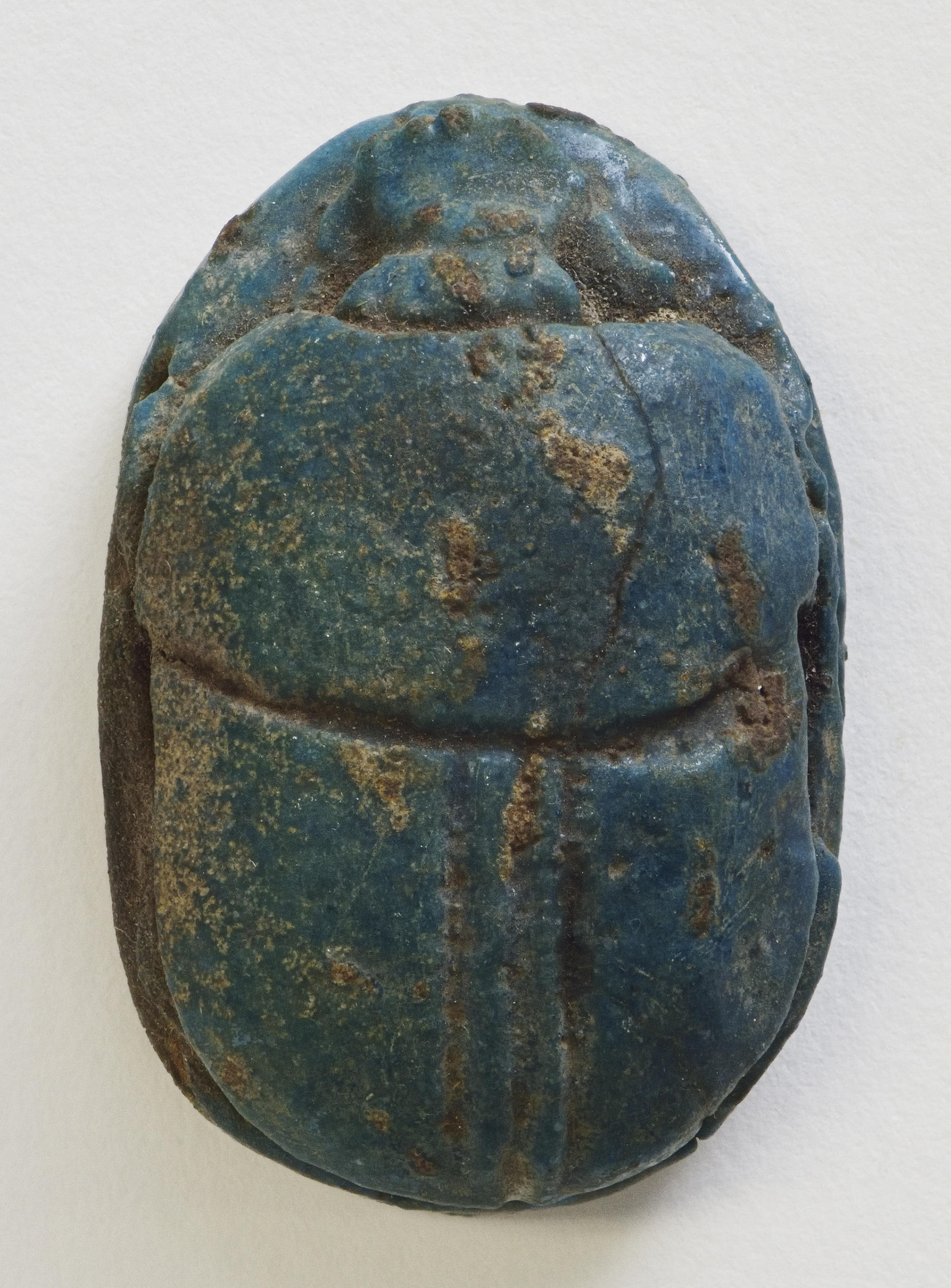 Carved scarab beetle figure in deep teal colors with six small holes on the underside of the beetle.
