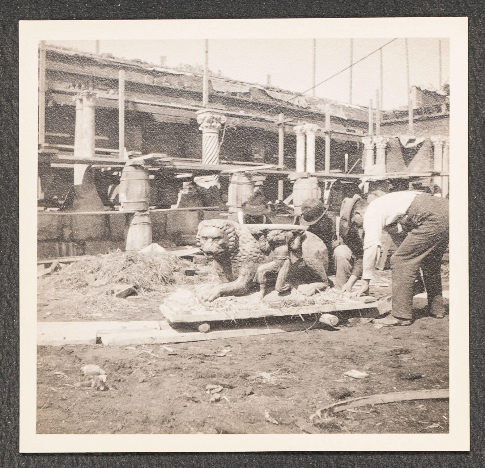 Black and white photographic print showing laborers working at the Fenway Court construction site moving a stone lion.