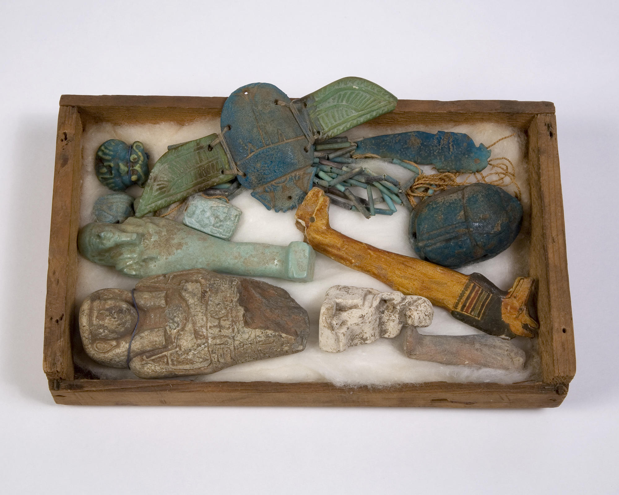 Rectangular wooden tray holding various carved statuettes, scarabs, and beads.