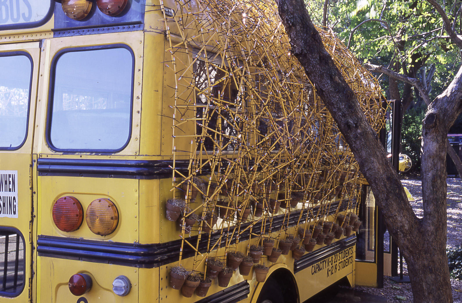 The outside of a yellow school bus with artist Nari Ward’s completed bramble of pencils, zipties, and flower pots.