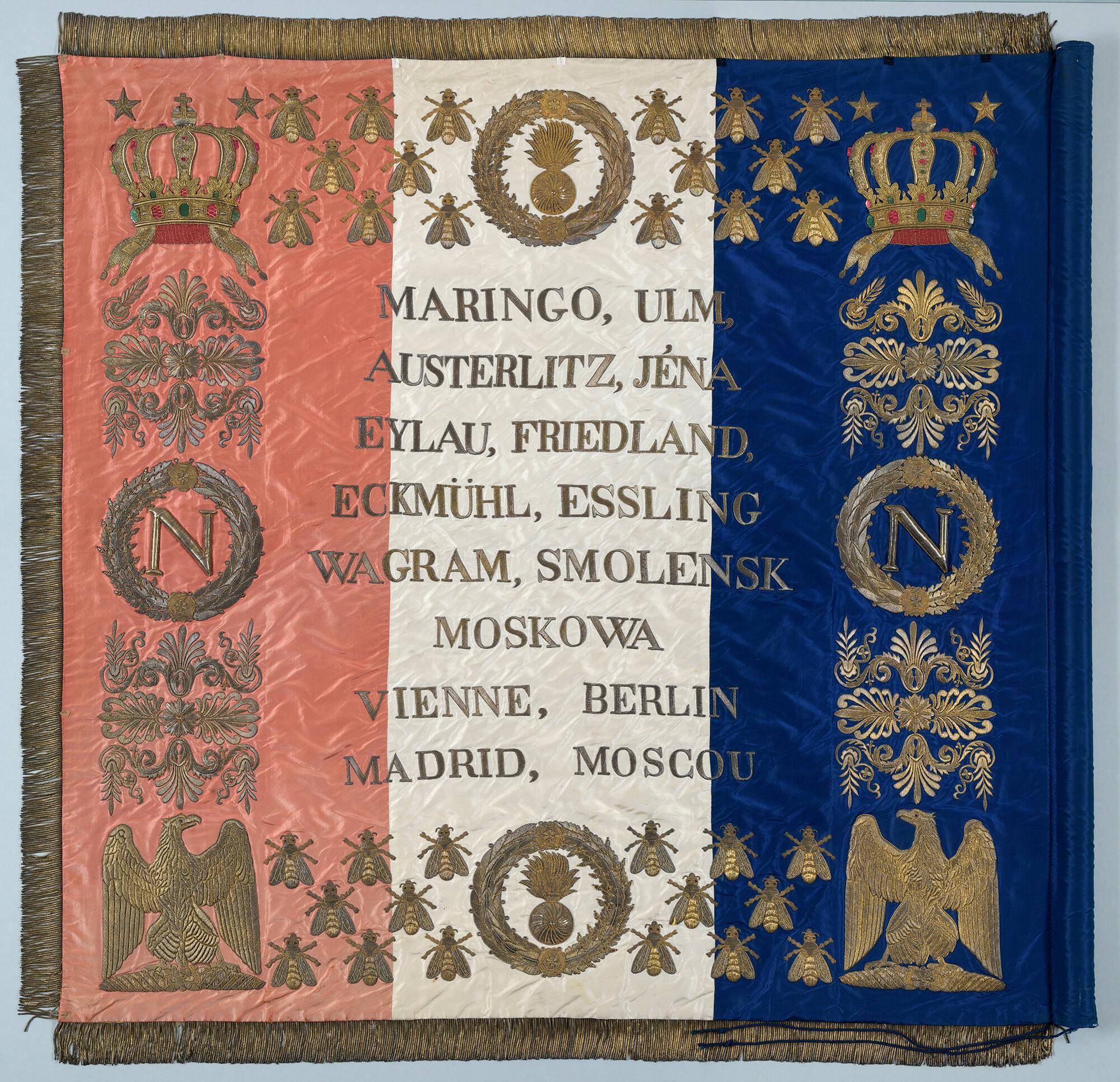 Back view of a square flag from Napoleon’s Imperial Guard embroidered in gold thread on blue, white, and red silk cloth, edged with gold fringe.