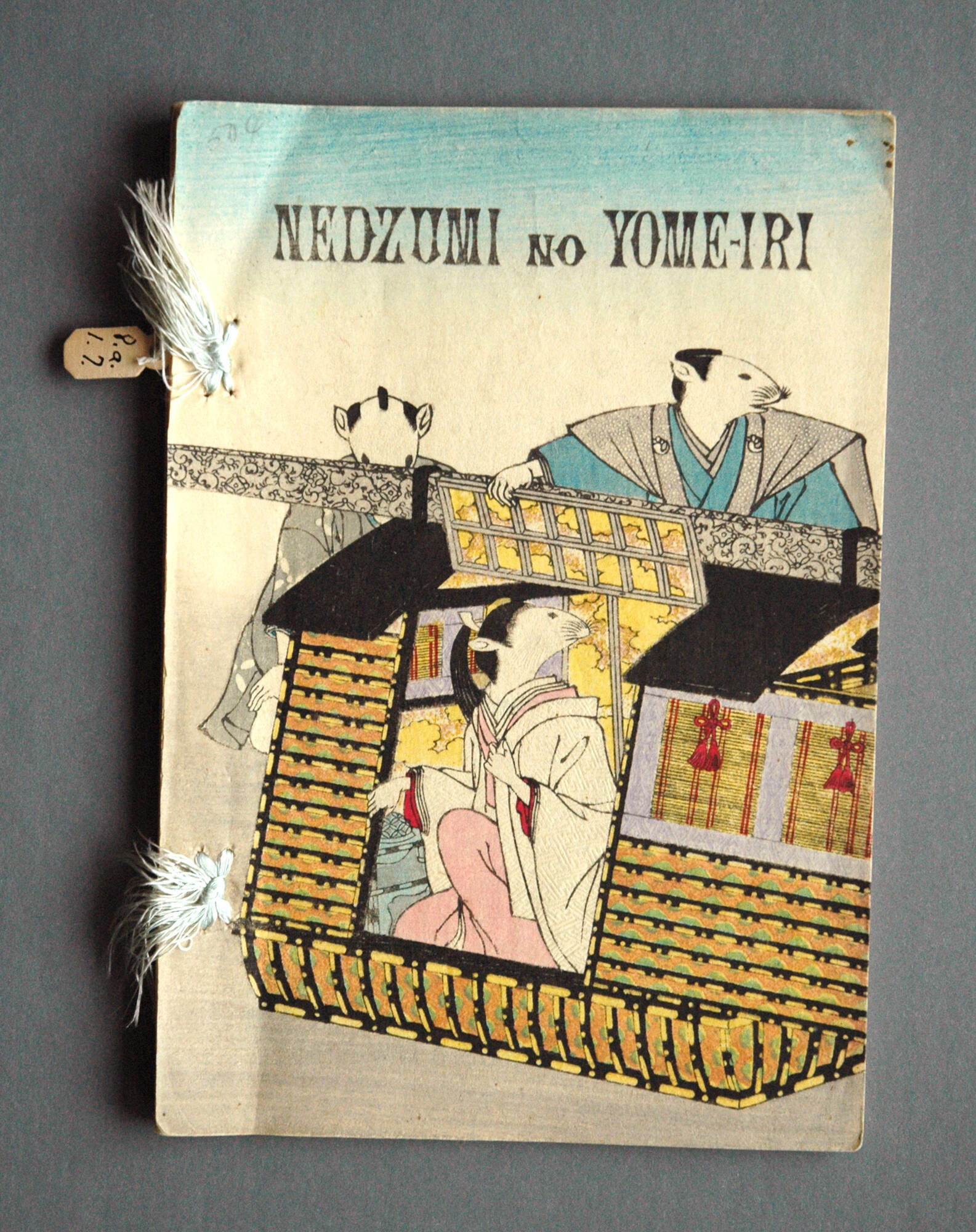 A photograph of a paperback copy of Nedzumi no Yome-iri with a color printed illustration on the cover of three anthropomorphized mice dressed in Japanese-style clothing.