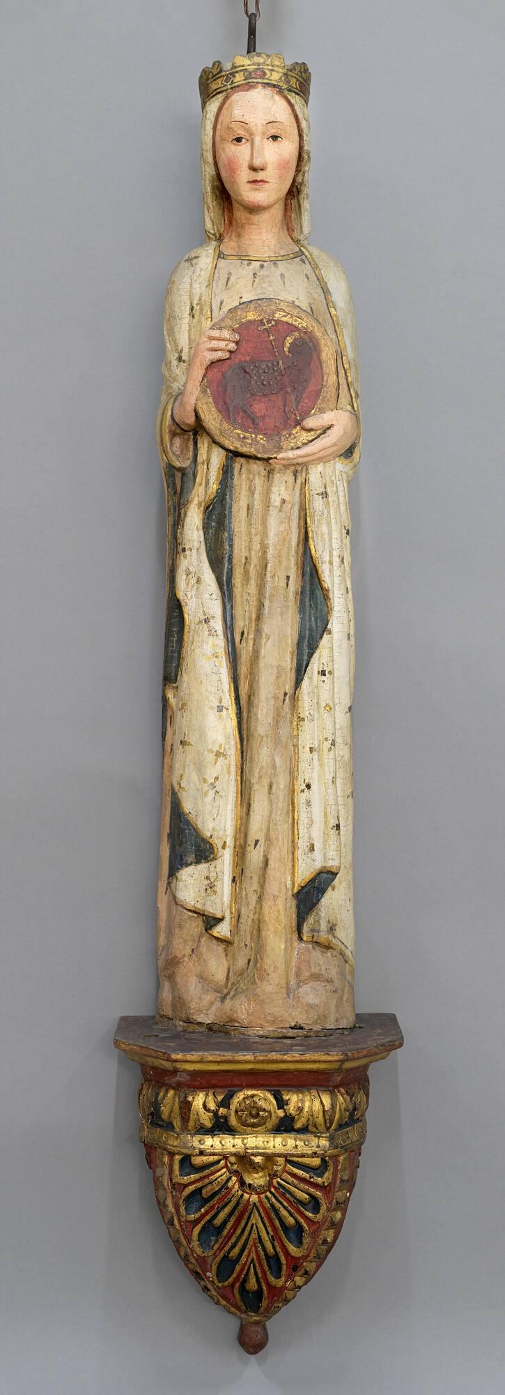 Painted and gilded wood sculpture of Saint Agnes, featuring a woman wearing a gold crown and white veil, robe and mantle with scattered gold decorations and a blue lining, while holding a red and gold medallion depicting a sheep with a gold halo and cross.
