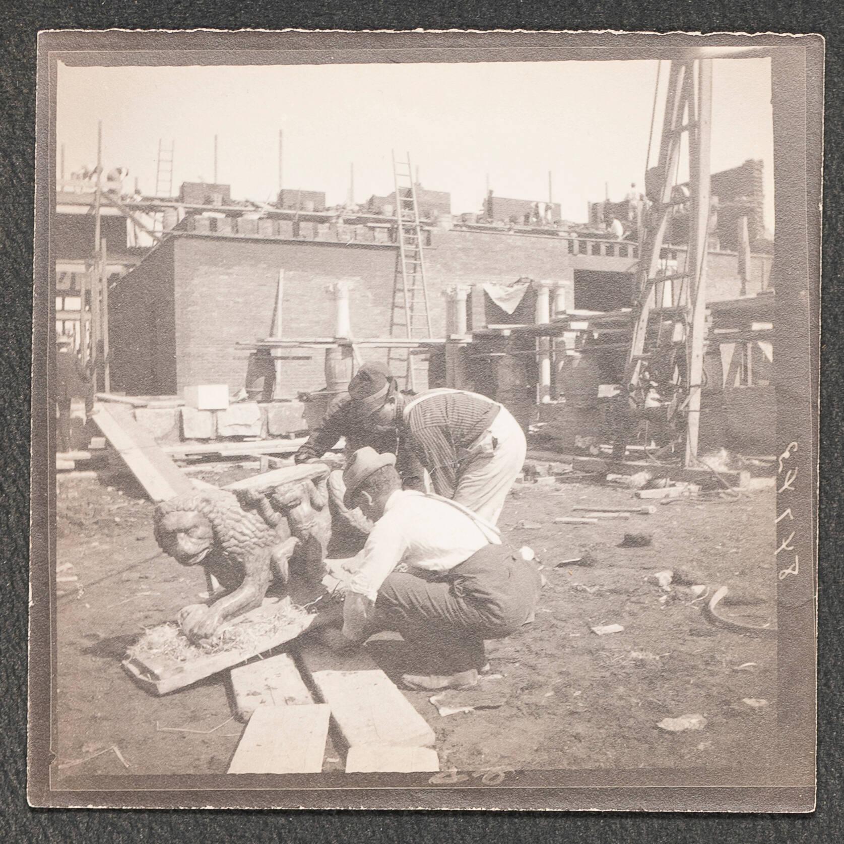 A black and white photograph of the Gardner Museum construction site with three men bent over picking up a stone sculpture of a lion.