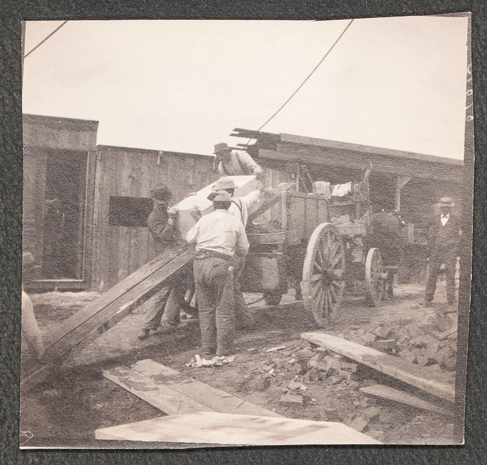 A black and white photograph of the Gardner Museum construction site with four workers loading an object onto a horse drawn carriage.