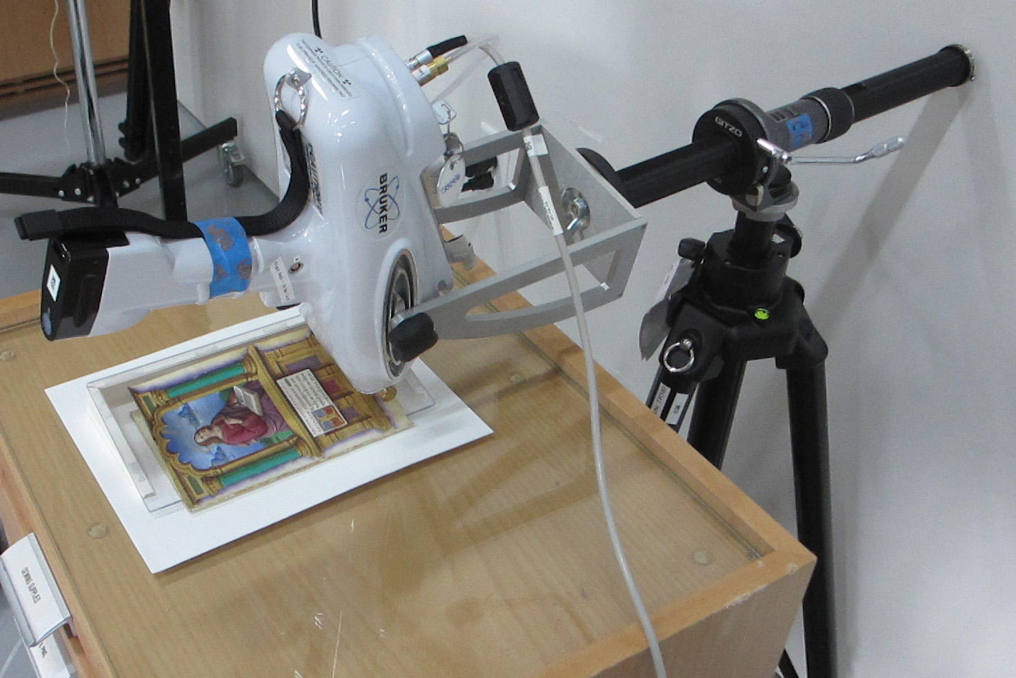 A portable XRF instrument, attached to a stand, points down to analyze a colorfully painted page from The Book of Hours by Jean Bourdichon.