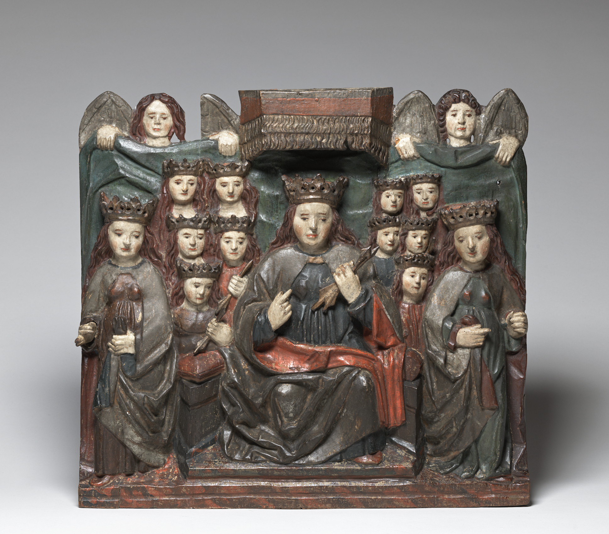 Painted wood sculpture of Saint Ursula and the Virgin Martyrs, featuring Saint Ursula crowned, enthroned and under a canopy at center surrounded by twelve crowned female figures of varying sizes, all set against a green curtain held at the top by two angels. 