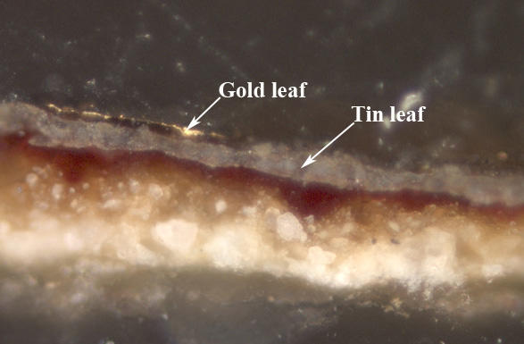 Magnified cross section sample from the Virgin Adoring the Christ Child showing  gilded and painted decoration with a thin layer of gold leaf on top of thicker layer of grayish tin leaf.  Below this is a thin layer of translucent deep red paint on top of a white gesso ground.