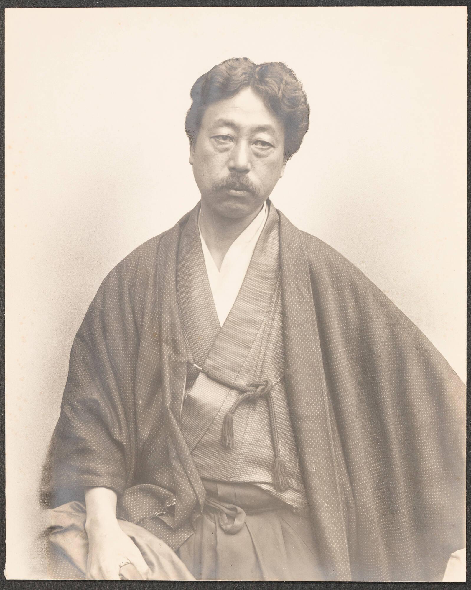 A black and white photograph of Okakura Kakuzō, who is a man with short hair, a mustache, and is wearing Japanese-style clothing.