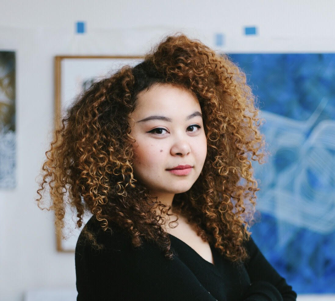Photo of a woman with curly hair in front of a blue painting.
