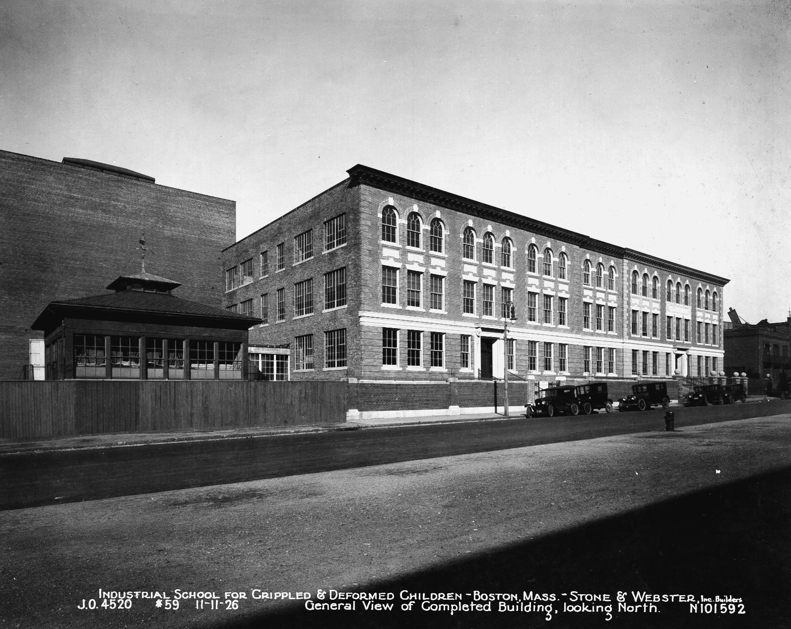 Three story Italianate stone and brick building on St. Botolph Street, home of Cotting School. Outdoor classroom and play yard adjacent to school. 