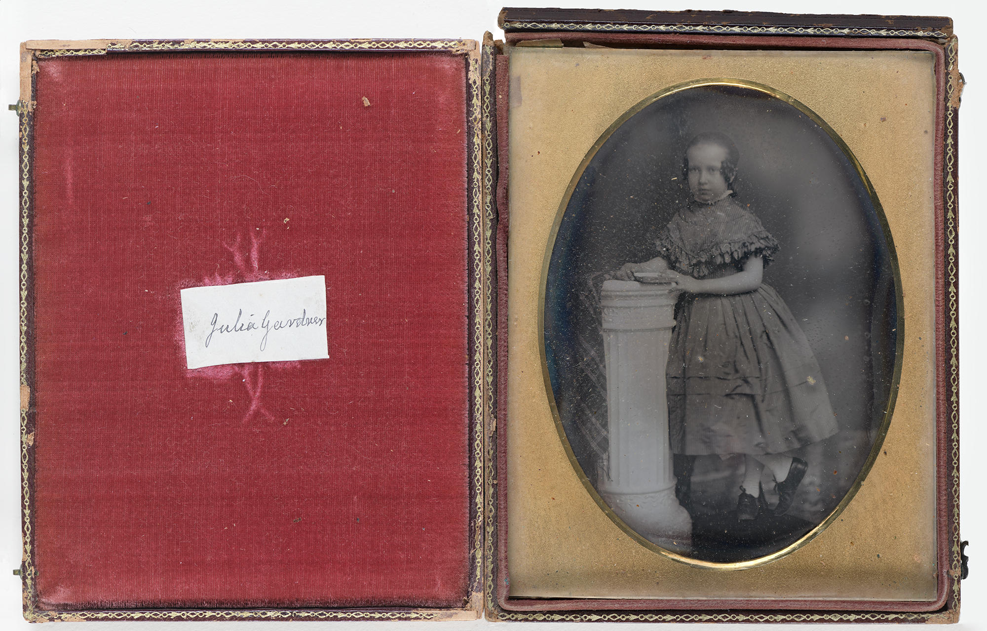 An open case lined with red velvet contains an oval black and white photograph of a girl about 9 years old identified as Julia Gardner. She is standing and wearing a 19th century dress and hairstyle.
