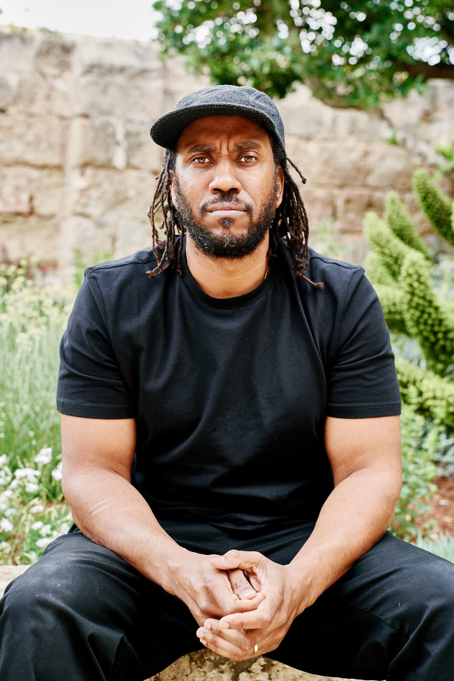 Photo of a person in a black outfit sitting outside. 