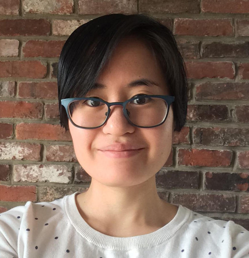 Photo of a person with glasses standing against a brick wall. 
