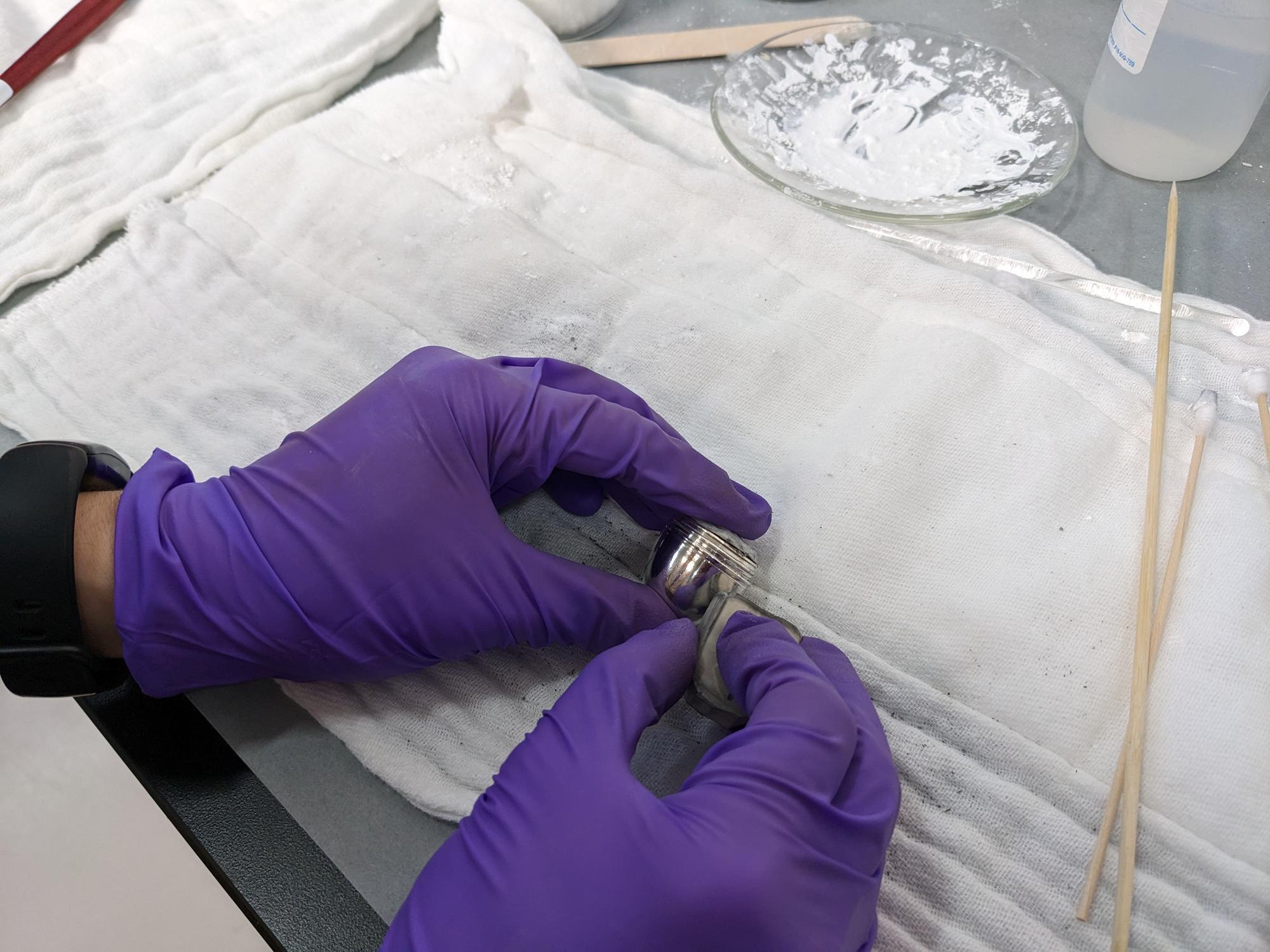 Image of a small silver object being cleaned by a staff member at the Isabella Stewart Gardner Museum while wearing nitrile gloves.